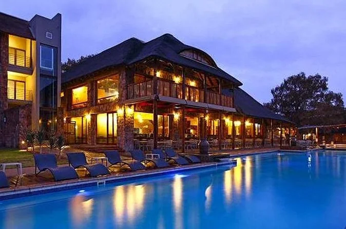Eine Safari-Lodge mit beleuchtetem Pool in der Abenddämmerung